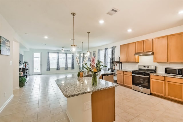 kitchen featuring a kitchen island, appliances with stainless steel finishes, plenty of natural light, pendant lighting, and light stone countertops