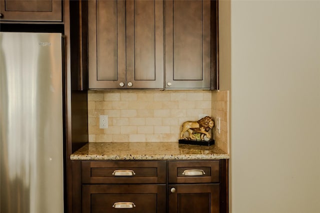 kitchen featuring decorative backsplash, stainless steel fridge, light stone countertops, and dark brown cabinets