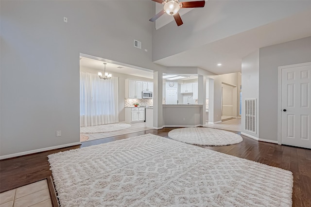 living room with ceiling fan with notable chandelier, high vaulted ceiling, and hardwood / wood-style flooring