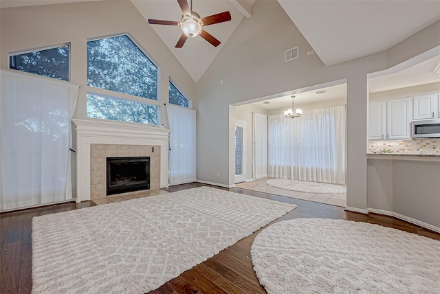 bedroom featuring hardwood / wood-style flooring, high vaulted ceiling, ceiling fan with notable chandelier, and a tile fireplace