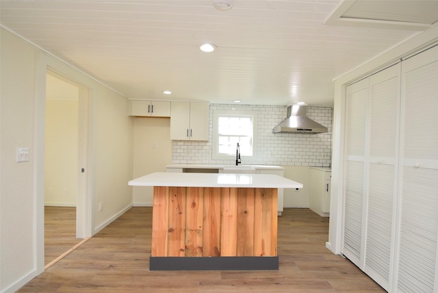 kitchen with wall chimney exhaust hood, a center island, white cabinets, and light wood-type flooring