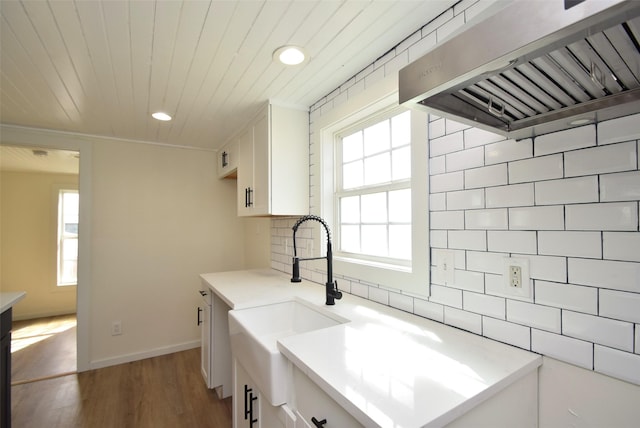 kitchen with tasteful backsplash, wall chimney range hood, sink, and white cabinets