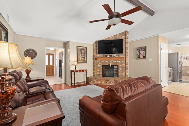 living room featuring ceiling fan, light hardwood / wood-style floors, a brick fireplace, and vaulted ceiling with beams