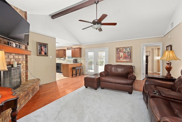 living room with french doors, vaulted ceiling with beams, ceiling fan, a fireplace, and light hardwood / wood-style floors