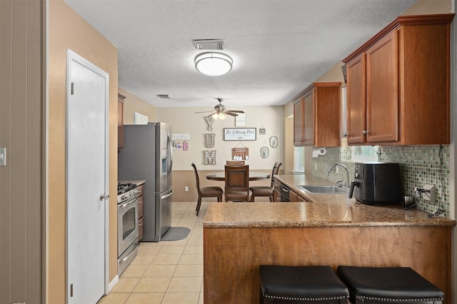 kitchen featuring appliances with stainless steel finishes, tasteful backsplash, sink, light tile patterned floors, and kitchen peninsula