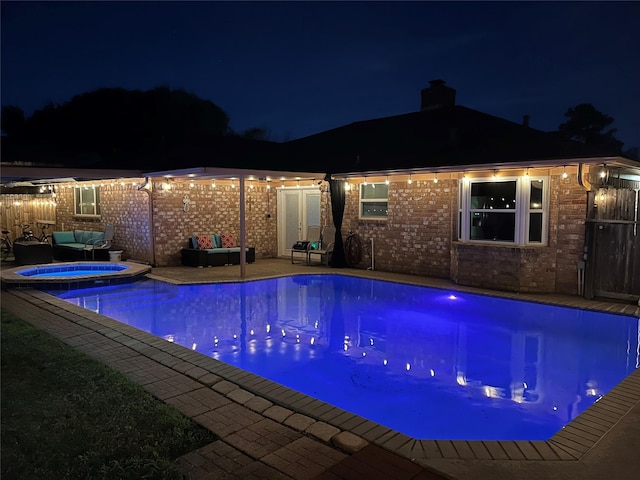 pool at night featuring a patio area and an in ground hot tub