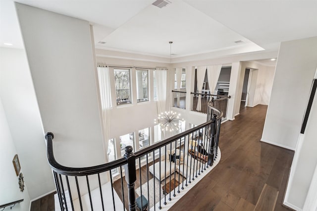 hall with a notable chandelier, a tray ceiling, and dark wood-type flooring