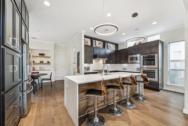 kitchen with sink, stainless steel appliances, dark brown cabinetry, an island with sink, and decorative light fixtures