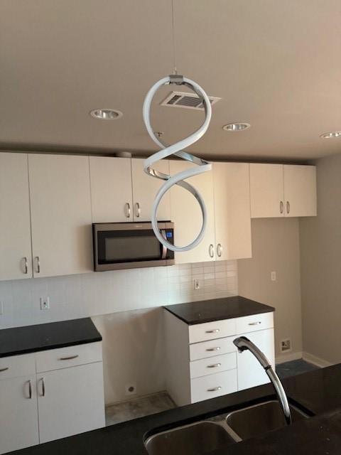 kitchen with hanging light fixtures, sink, white cabinets, and backsplash