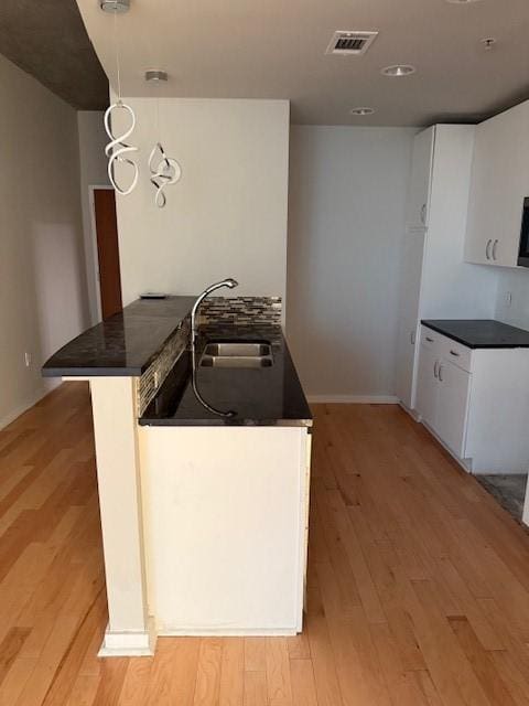 kitchen featuring sink, kitchen peninsula, pendant lighting, light hardwood / wood-style floors, and white cabinets