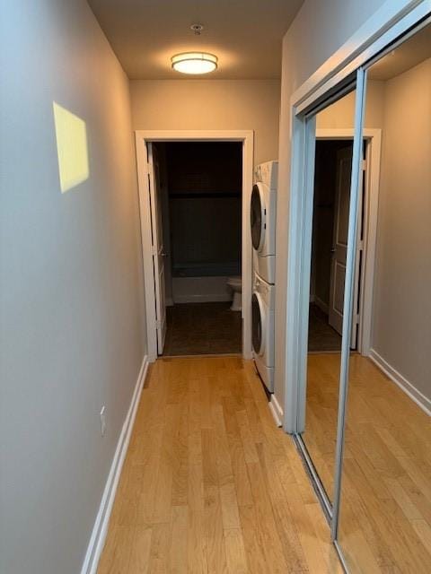 hall with stacked washer and clothes dryer and light wood-type flooring