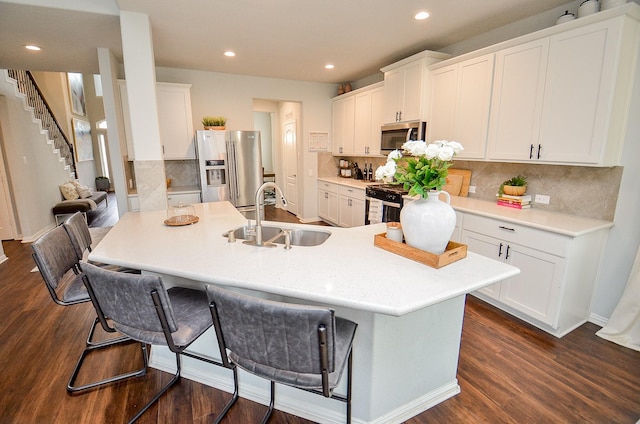 kitchen with sink, a breakfast bar area, appliances with stainless steel finishes, white cabinetry, and dark hardwood / wood-style flooring