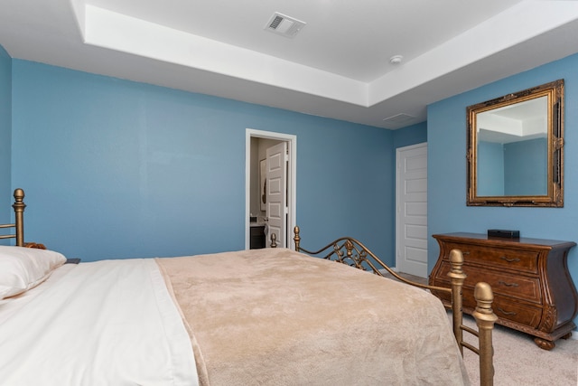 bedroom with a raised ceiling, ensuite bathroom, and light carpet