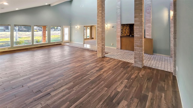 unfurnished living room with hardwood / wood-style floors, high vaulted ceiling, and ornate columns