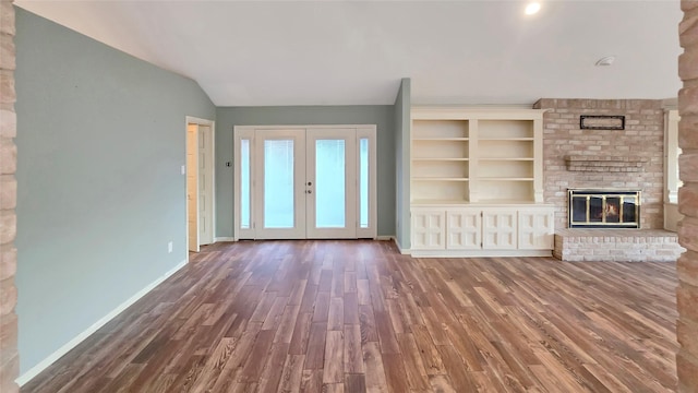 unfurnished living room featuring vaulted ceiling, a brick fireplace, dark wood-type flooring, and french doors