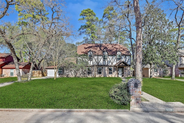 tudor-style house with a garage, an outdoor structure, and a front yard