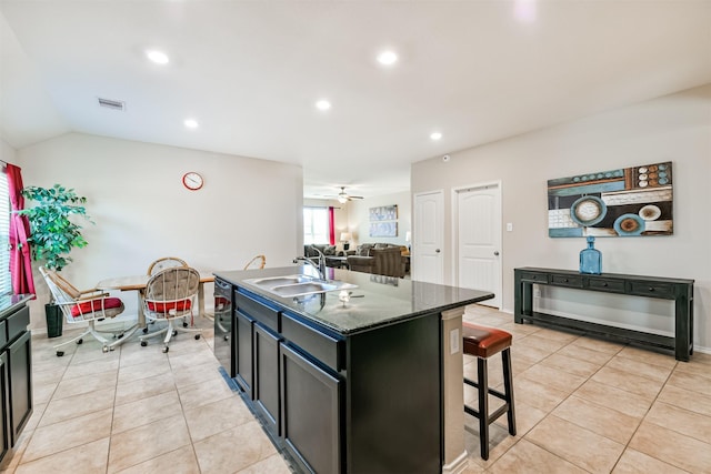 kitchen with vaulted ceiling, a center island with sink, a kitchen bar, and light tile patterned floors