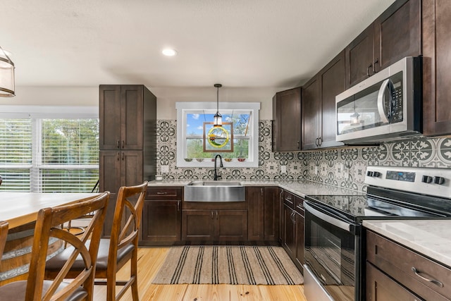 kitchen featuring appliances with stainless steel finishes, pendant lighting, tasteful backsplash, sink, and light hardwood / wood-style floors