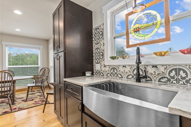 kitchen with sink, light hardwood / wood-style flooring, backsplash, dark brown cabinetry, and light stone countertops