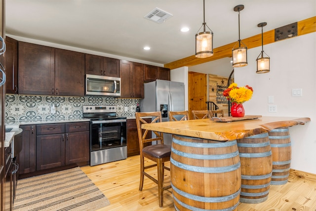 kitchen with a breakfast bar area, light hardwood / wood-style flooring, appliances with stainless steel finishes, kitchen peninsula, and decorative backsplash