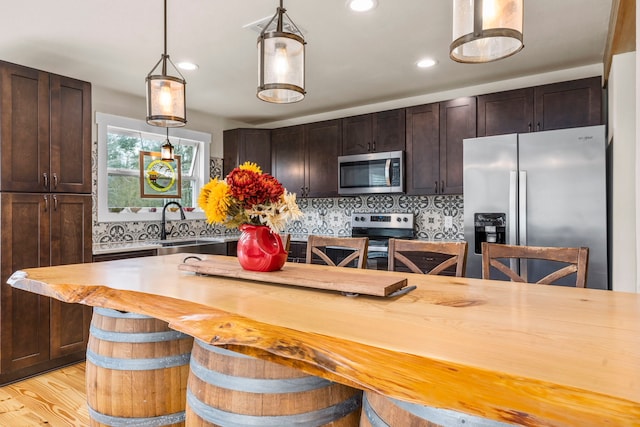 kitchen featuring dark brown cabinetry, decorative backsplash, stainless steel appliances, and a kitchen breakfast bar