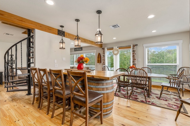 bar featuring beamed ceiling, plenty of natural light, decorative light fixtures, and light hardwood / wood-style floors