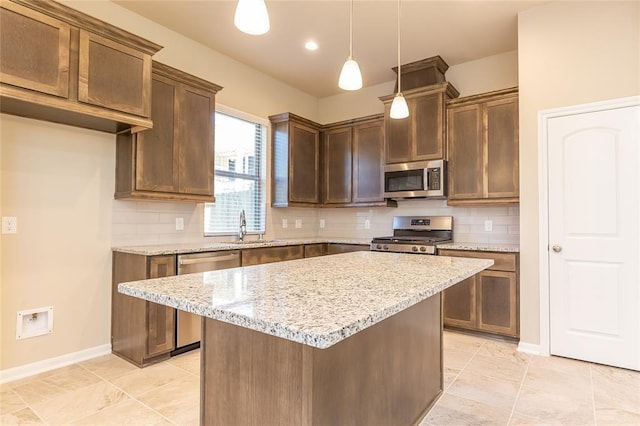 kitchen with appliances with stainless steel finishes, decorative light fixtures, tasteful backsplash, a center island, and light stone counters