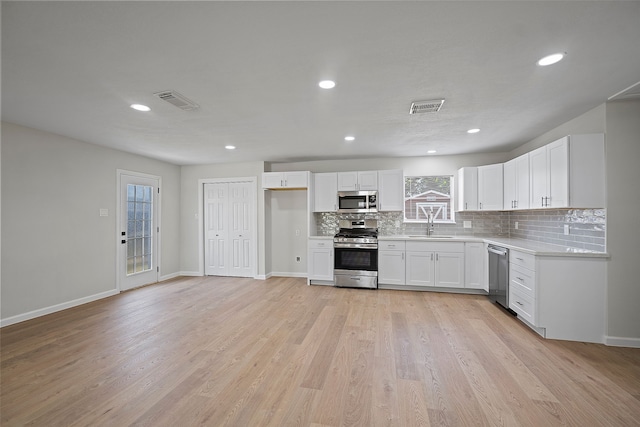 kitchen with sink, light wood-type flooring, stainless steel appliances, decorative backsplash, and white cabinets