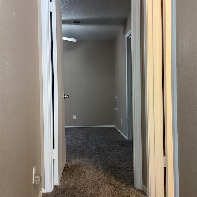 corridor with a textured ceiling and dark carpet