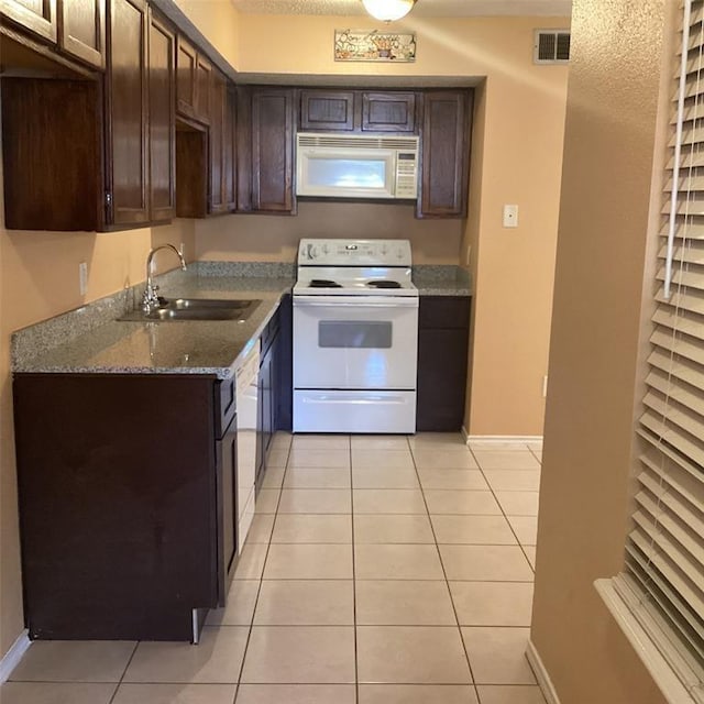 kitchen featuring light tile patterned flooring, dark brown cabinetry, sink, white appliances, and light stone countertops