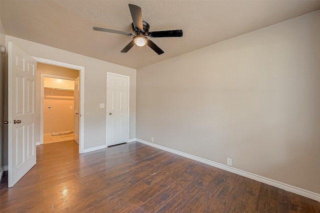 unfurnished bedroom with ceiling fan, a textured ceiling, dark hardwood / wood-style flooring, a spacious closet, and a closet