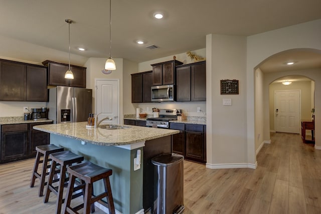 kitchen featuring decorative light fixtures, sink, a kitchen island with sink, stainless steel appliances, and dark brown cabinets