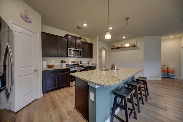 kitchen with appliances with stainless steel finishes, a kitchen bar, hanging light fixtures, a kitchen island with sink, and dark brown cabinets