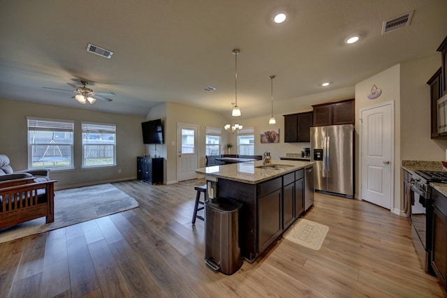 kitchen featuring appliances with stainless steel finishes, decorative light fixtures, a center island, light hardwood / wood-style floors, and dark brown cabinets