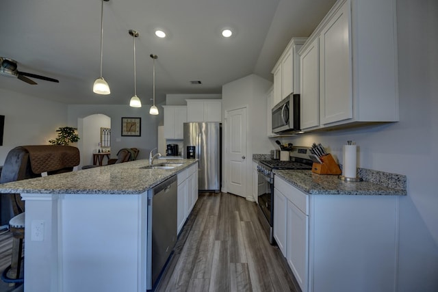 kitchen with appliances with stainless steel finishes, a center island with sink, white cabinets, and decorative light fixtures