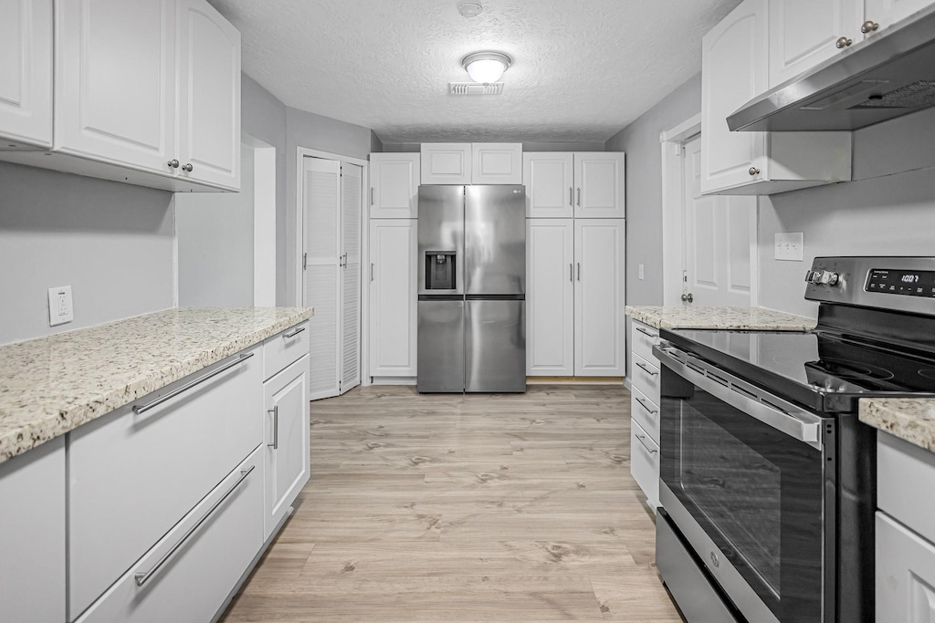 kitchen with appliances with stainless steel finishes, white cabinetry, light stone counters, light hardwood / wood-style floors, and a textured ceiling