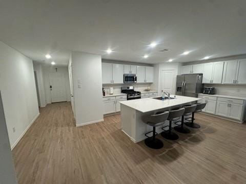 kitchen featuring sink, appliances with stainless steel finishes, white cabinetry, a kitchen breakfast bar, and an island with sink