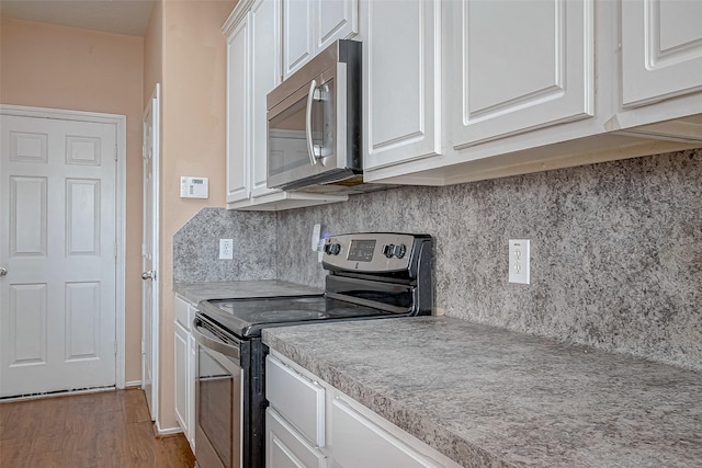 kitchen with decorative backsplash, light hardwood / wood-style flooring, white cabinets, and appliances with stainless steel finishes