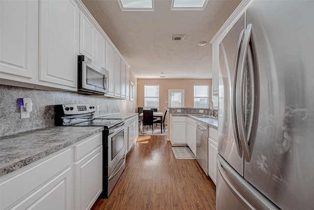 kitchen with white cabinetry, stainless steel appliances, sink, and light hardwood / wood-style flooring