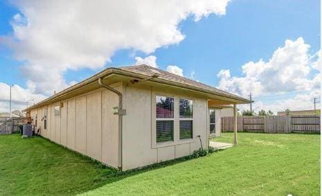 view of side of home with central AC and a yard