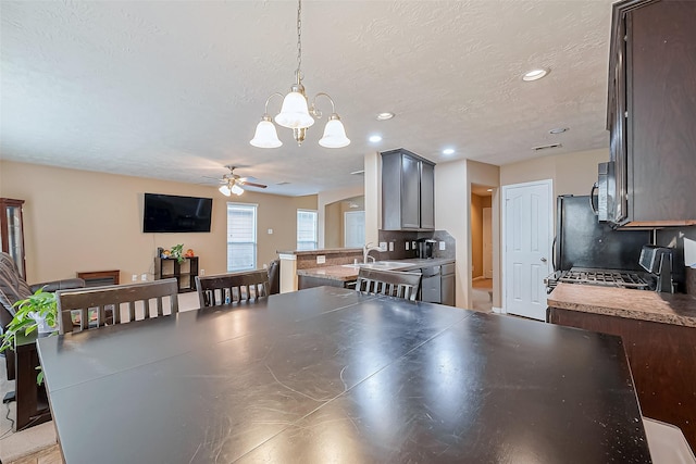 dining space with sink, ceiling fan with notable chandelier, and a textured ceiling