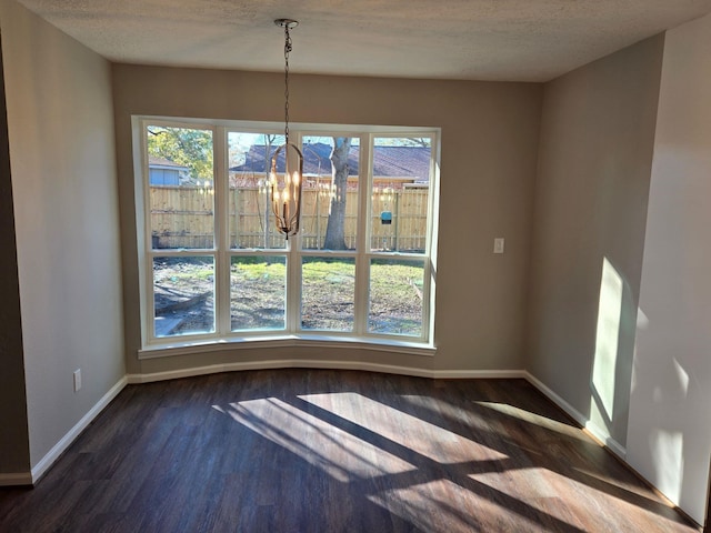 unfurnished dining area with dark wood-type flooring, a chandelier, and a textured ceiling