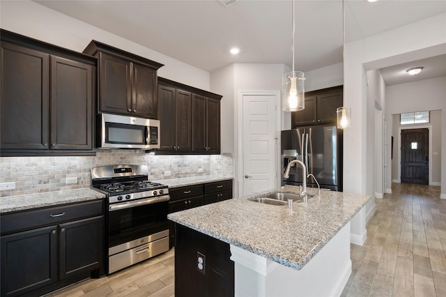 kitchen with sink, light stone counters, a center island with sink, stainless steel appliances, and backsplash