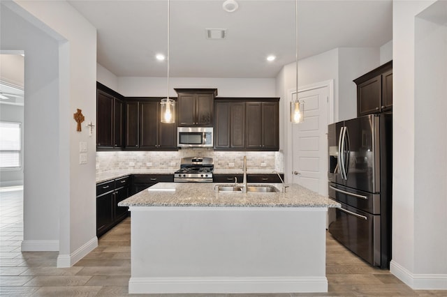 kitchen with sink, stainless steel appliances, hanging light fixtures, and a center island with sink