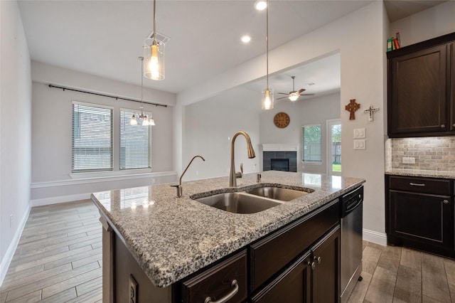 kitchen featuring dishwasher, sink, light stone counters, dark brown cabinetry, and a center island with sink