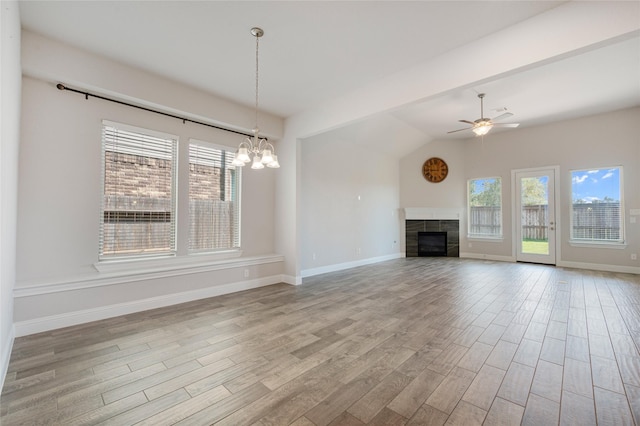 unfurnished living room with lofted ceiling, ceiling fan with notable chandelier, and a tile fireplace