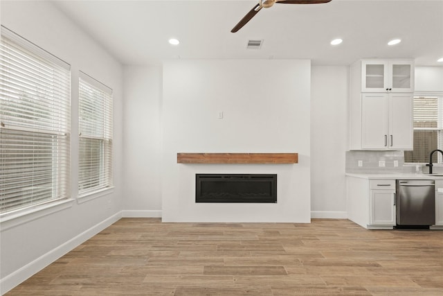 unfurnished living room featuring ceiling fan, a healthy amount of sunlight, sink, and light wood-type flooring