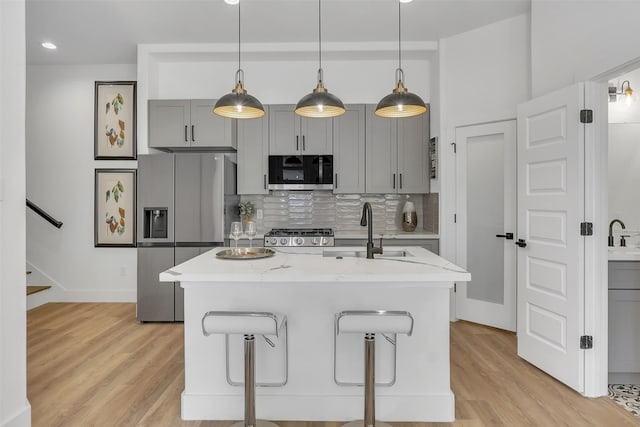 kitchen featuring gray cabinets, a breakfast bar, stainless steel appliances, light stone counters, and decorative backsplash