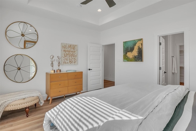 bedroom with ensuite bath, a tray ceiling, ceiling fan, and light hardwood / wood-style floors