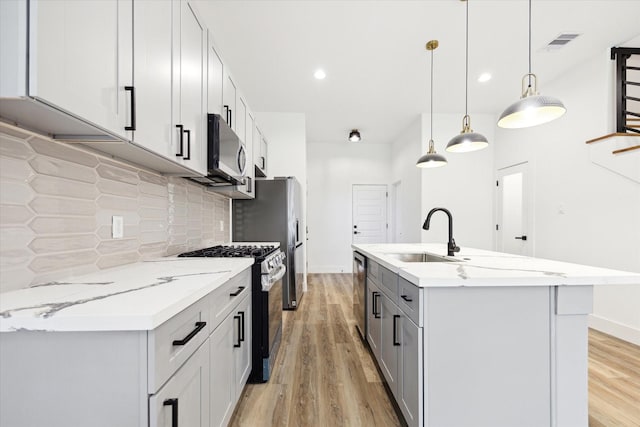 kitchen with appliances with stainless steel finishes, decorative light fixtures, an island with sink, sink, and backsplash